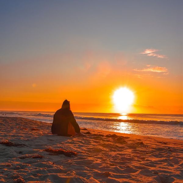 Person meditating peacefully near a calm lake with sun rays